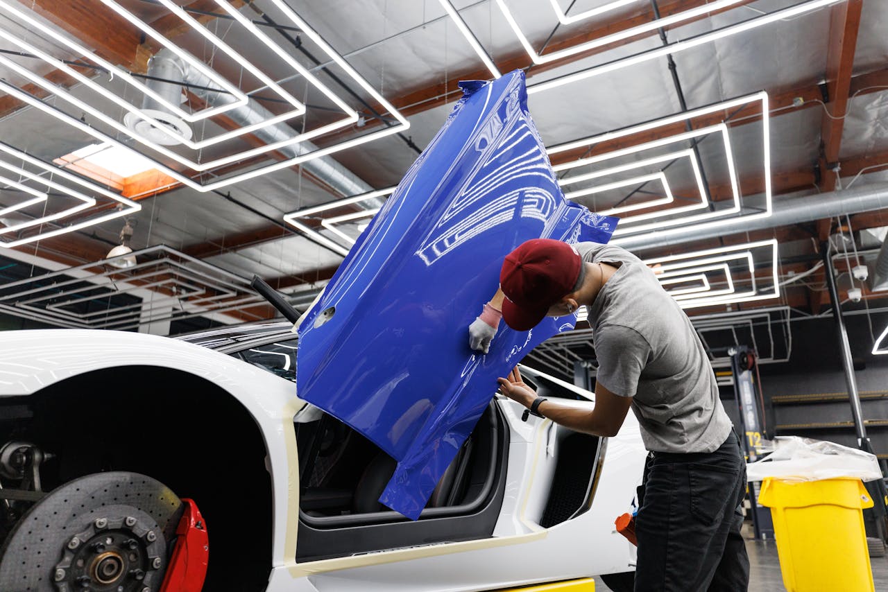 gallery-02 Auto mechanic applying blue vinyl wrap to a car door in a modern garage.