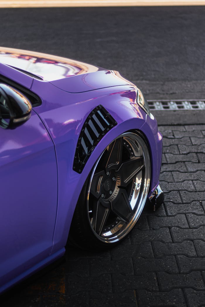gallery-05 Close-up view of a purple cars front wheel showcasing sleek design and vibrant color.