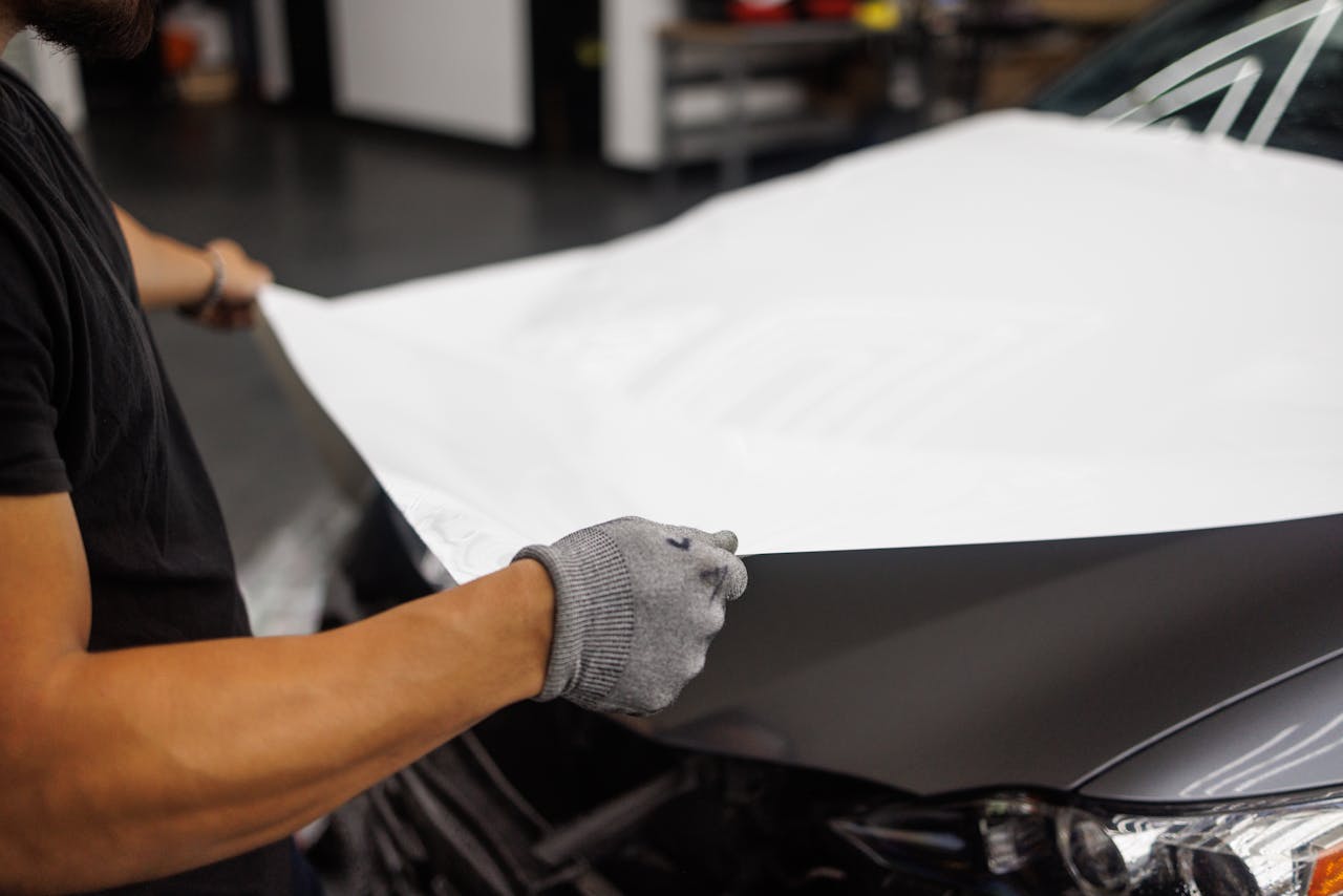 gallery-03 Person applying vinyl wrap to car hood in garage setting.